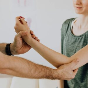Crop unrecognizable chiropractor examining arm of smiling female patient
